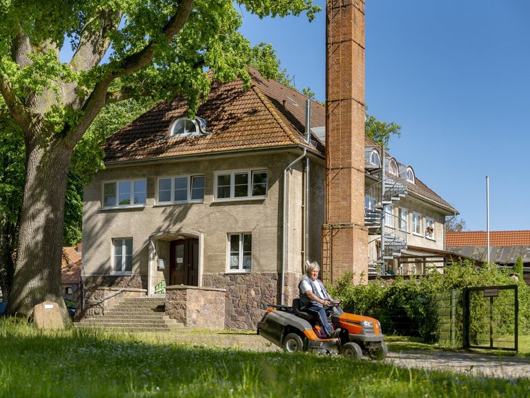 Frontansicht des Hauses und eine Person die den Rasen mäht.